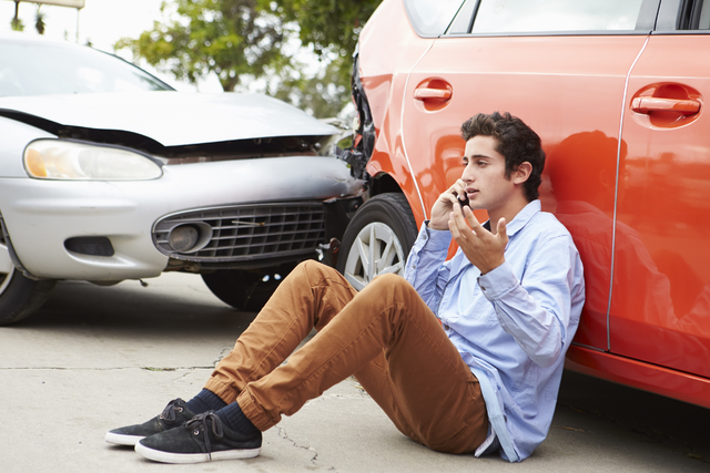 Young man on phone and wrecked car